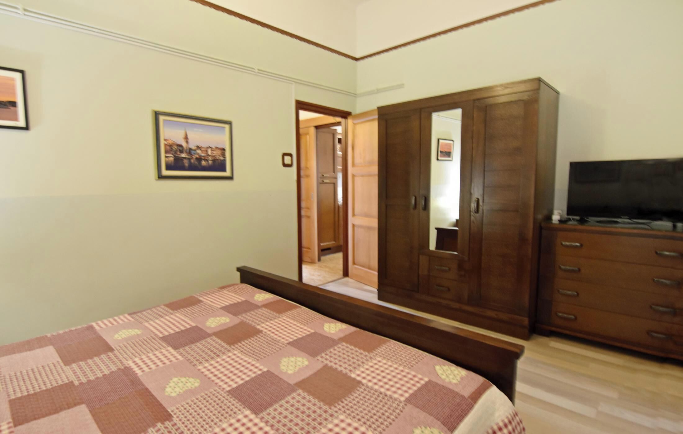 Un dormitorio con cama, armario, televisor y un cuadro en la pared.