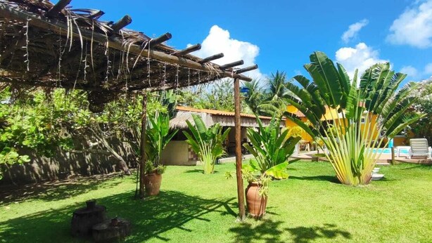 Ein tropischer Garten mit einem Reetdachhaus, einem Poolbereich und üppiger Vegetation.