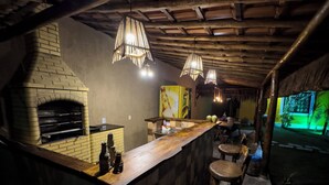 Eine rustikale Bar mit Backofen, Holzbalkendecke, hängenden Lampen und Außenplätzen.