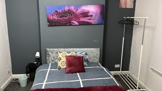 Et soveværelse med seng, sengebord, lampe og et billede på væggen.