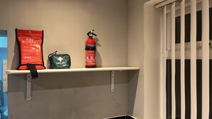 En hylde med et brandtæppe, et førstehjælpskit og en brandslukker.