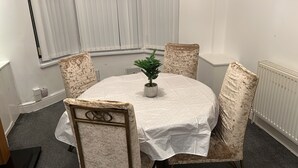 Et rundt bord med hvid dug, fire polstrede stole og en potteplante i midten.