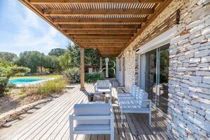 A wooden deck with outdoor seating, a pool, and a stone building.