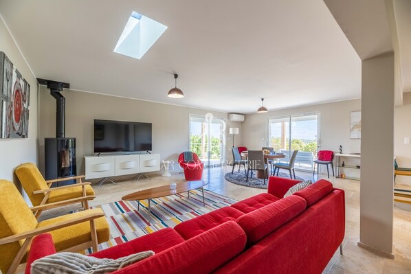 A modern living room with a large flat-screen TV, a red sofa, and a dining area with a table and chairs.