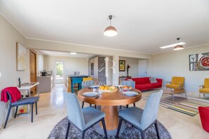 A modern living room with a dining area, red sofa, and a kitchen in the background.