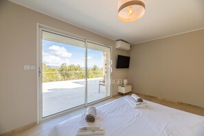 A hotel room with a large sliding glass door leading to an outdoor terrace, a flat-screen TV mounted on the wall, and neatly folded towels on the bed.