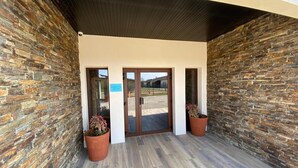A building entrance with a stone facade, a wooden floor, and two potted plants. - WORLD HOTEL (Saint-Vulbas)
