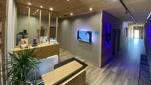 A modern reception area with a wooden reception desk, a large mirror, and a television screen. - WORLD HOTEL (Saint-Vulbas)