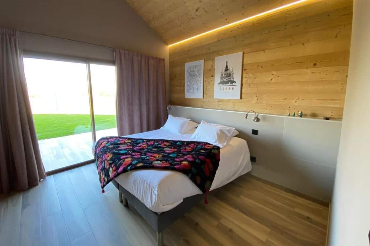 A bedroom with a bed, a window with curtains, wooden walls, and a ceiling light.