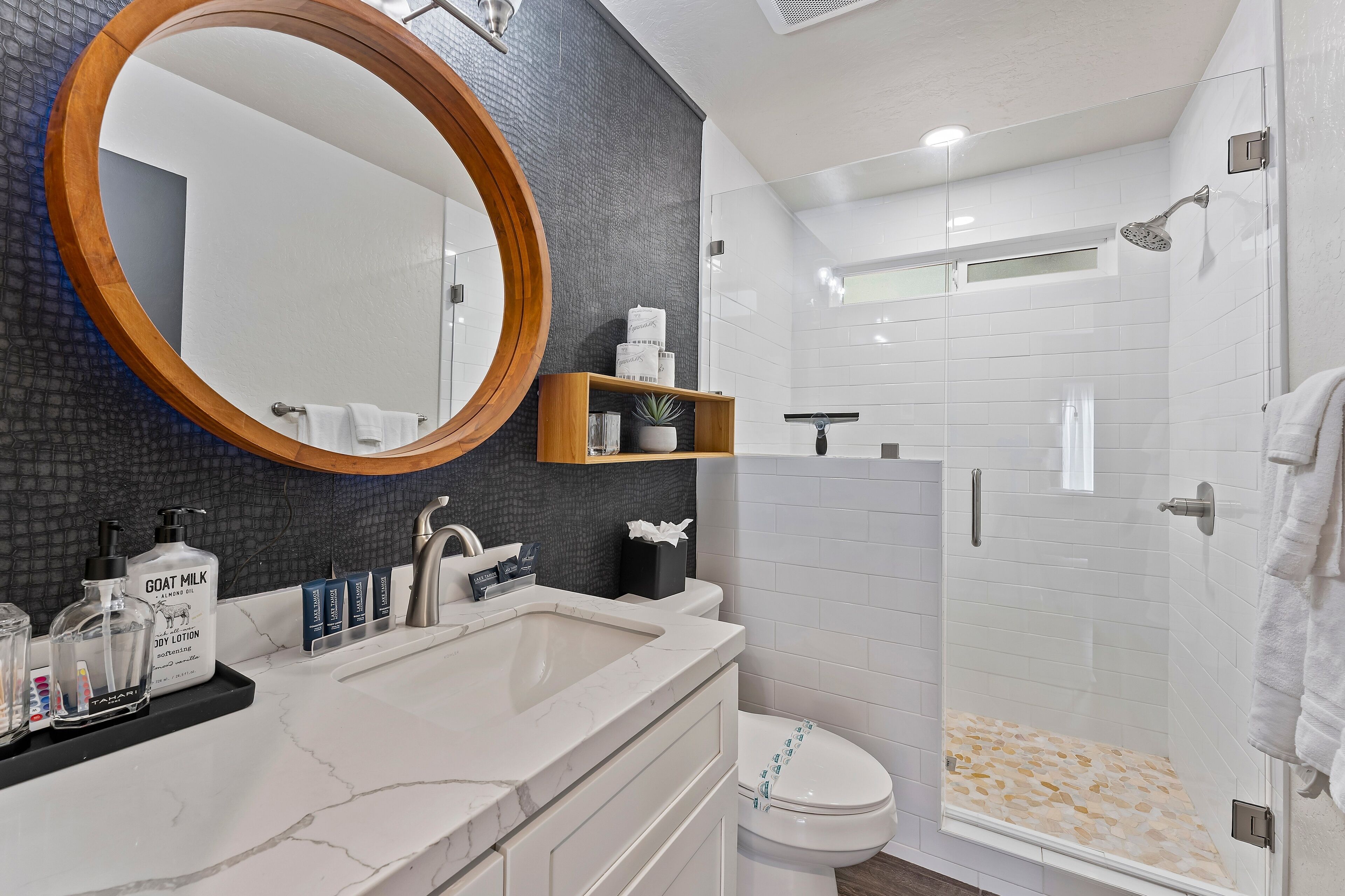 A modern bathroom with a large mirror, a white sink, a toilet, and a glass-enclosed shower.
