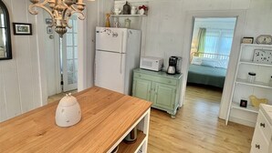 Une cuisine chaleureuse avec un plancher en bois, une table à manger en bois, un réfrigérateur blanc, un four à micro-ondes et un luminaire suspendu.