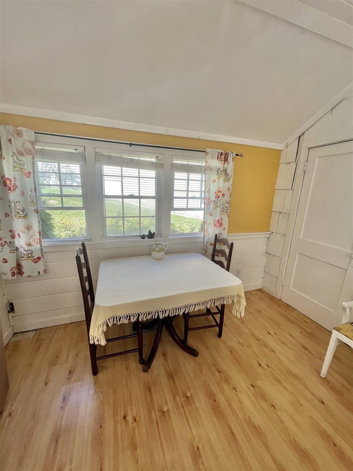 A dining area with a table and chairs, a window with curtains, and a door.