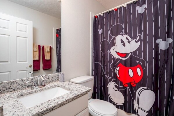 A bathroom with a Mickey Mouse shower curtain, a white toilet, and a granite countertop sink. - Irish Charm 6 Bedroom Home (Kissimmee)