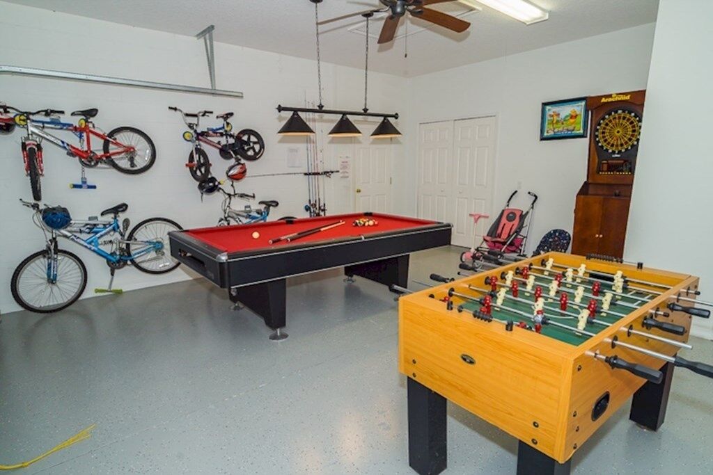 A room with a pool table, foosball table, bicycles, and a dartboard.