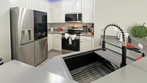 Una cucina moderna con mobili bianchi, elettrodomestici in acciaio inossidabile e lavello nero.