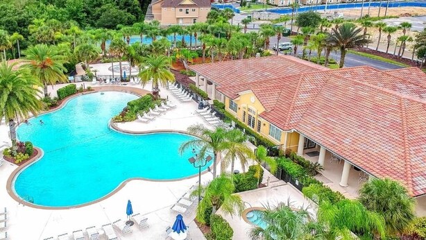 Una piscina con lettini e ombrelloni, circondata da palme e un edificio con tetto in tegole rosse.