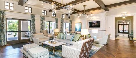 A spacious living room with a high ceiling, large windows, and a modern chandelier.