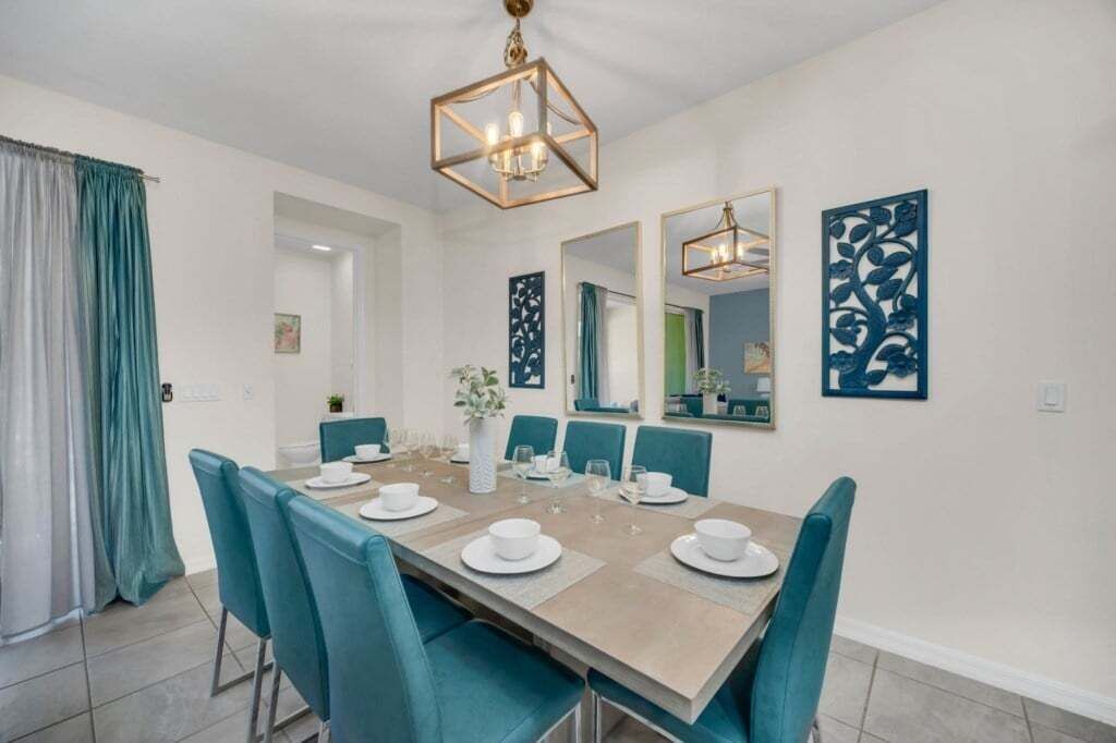 A dining area with a rectangular table set for six, teal chairs, and a chandelier.