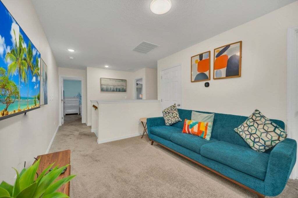 A living room with a teal sofa, a painting of a beach, and abstract art on the wall.