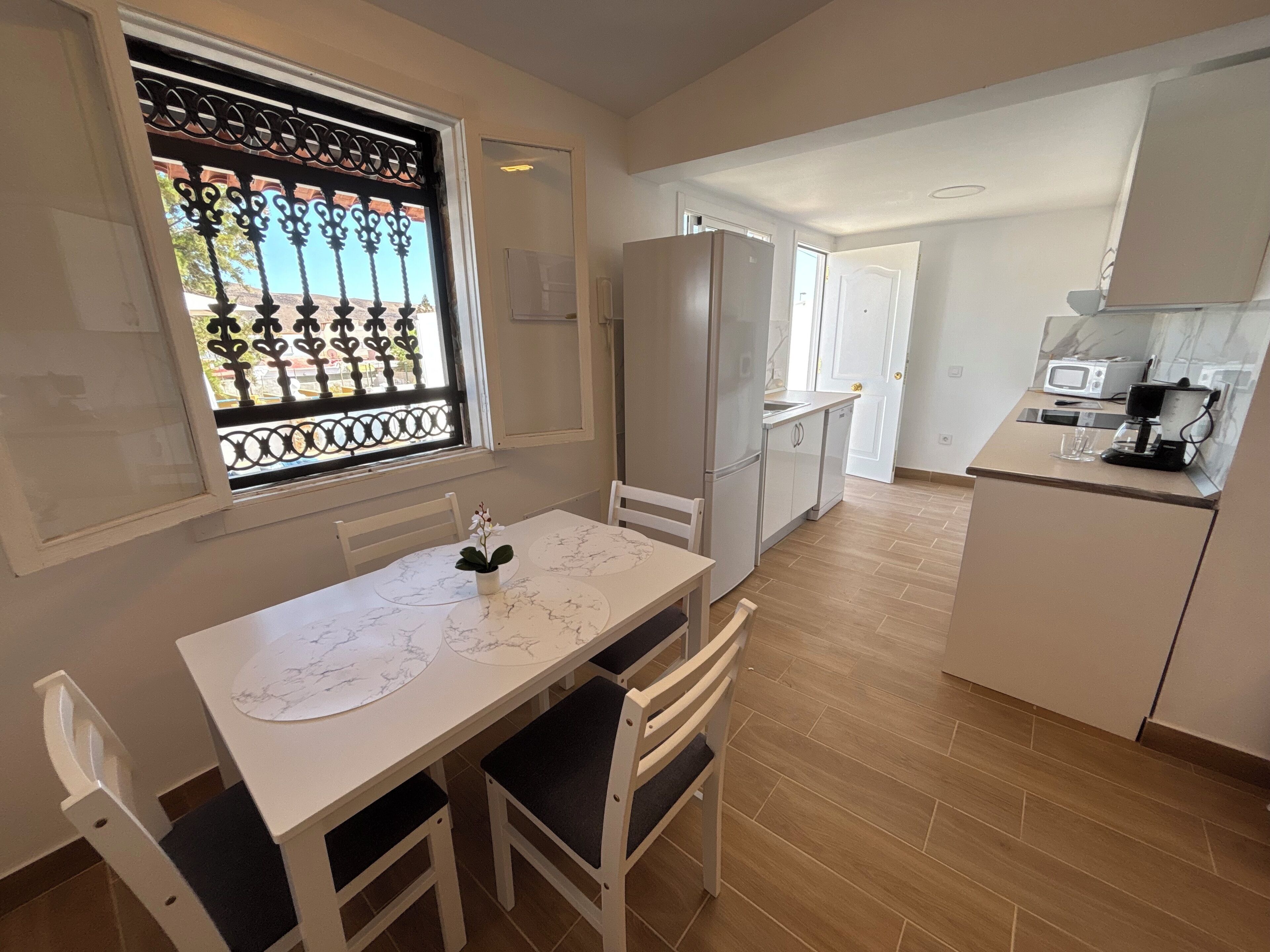 A compact kitchen with a marble countertop, a refrigerator, a microwave, and a coffee machine.