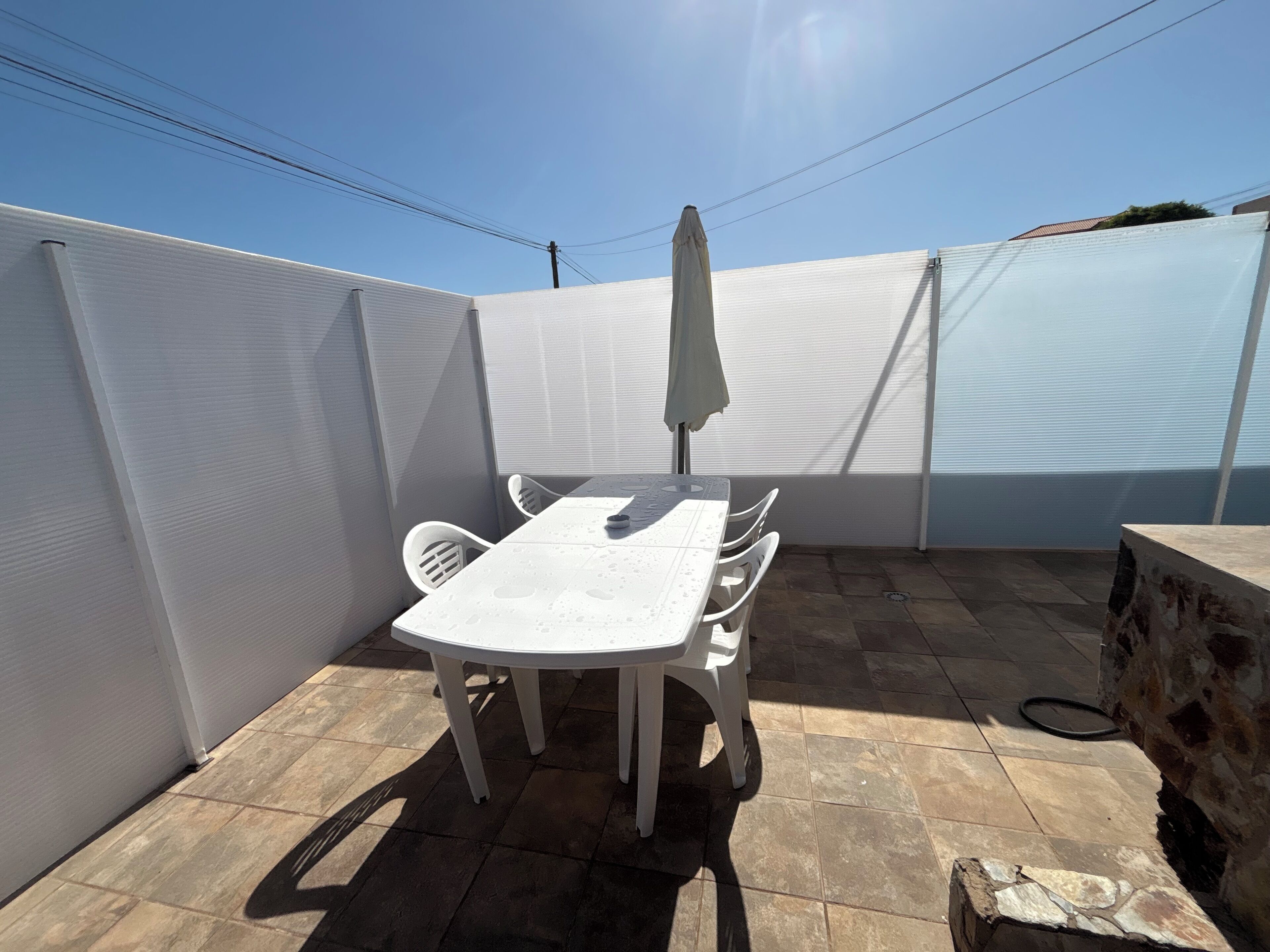 Een terras met een witte tafel en stoelen, een overdekte parasol en een stenen muur.