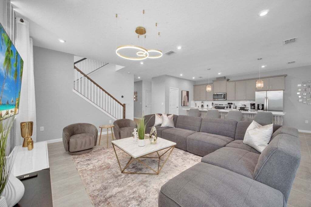 A modern living room with a sectional sofa, a coffee table, and a staircase leading to an upper floor.
