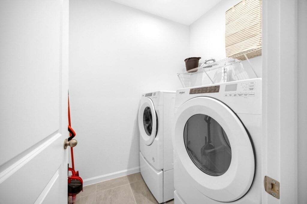A laundry room with two white front-loading washing machines, a red mop, and a basket on the wall.