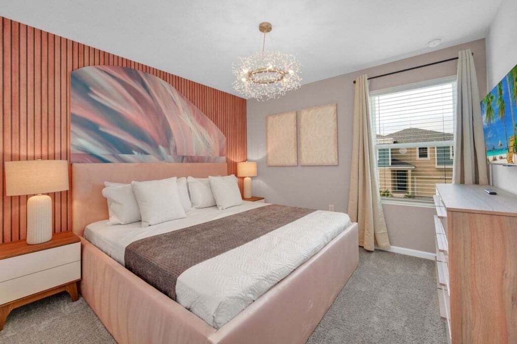 A modern bedroom with a large bed, a wooden headboard, a chandelier, and a view of the outside.