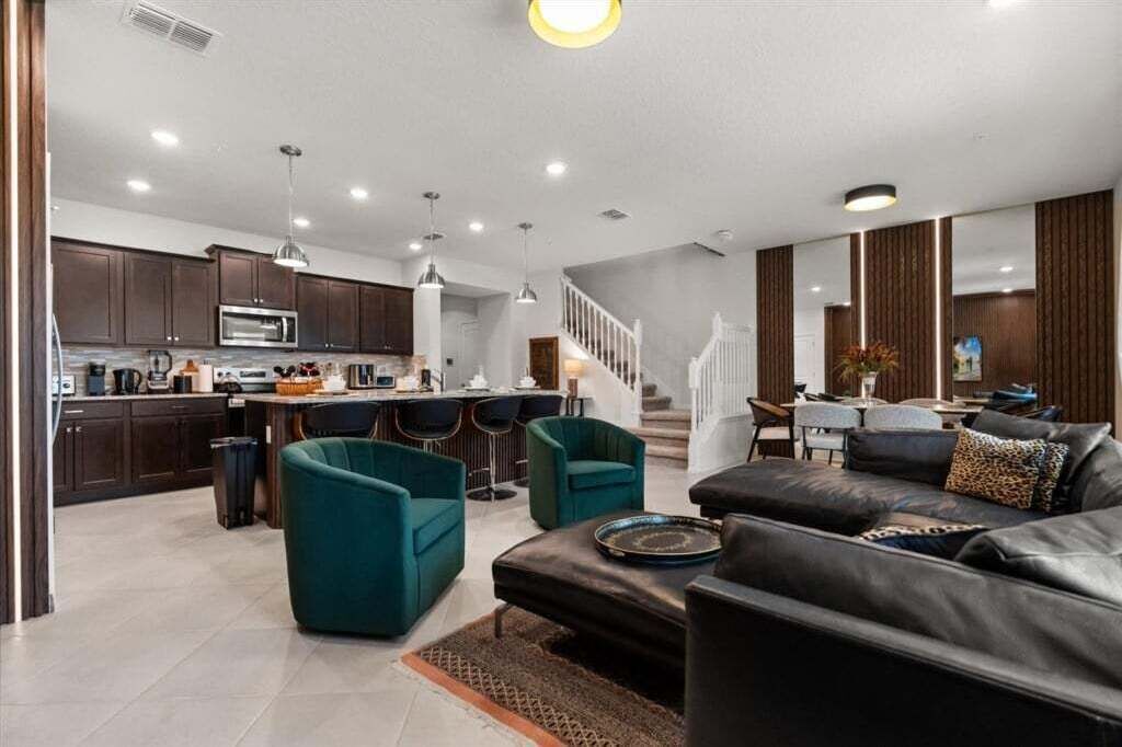 Un salon moderne avec un canapé en cuir noir, des fauteuils turquoise et un coin repas doté d’un bar.