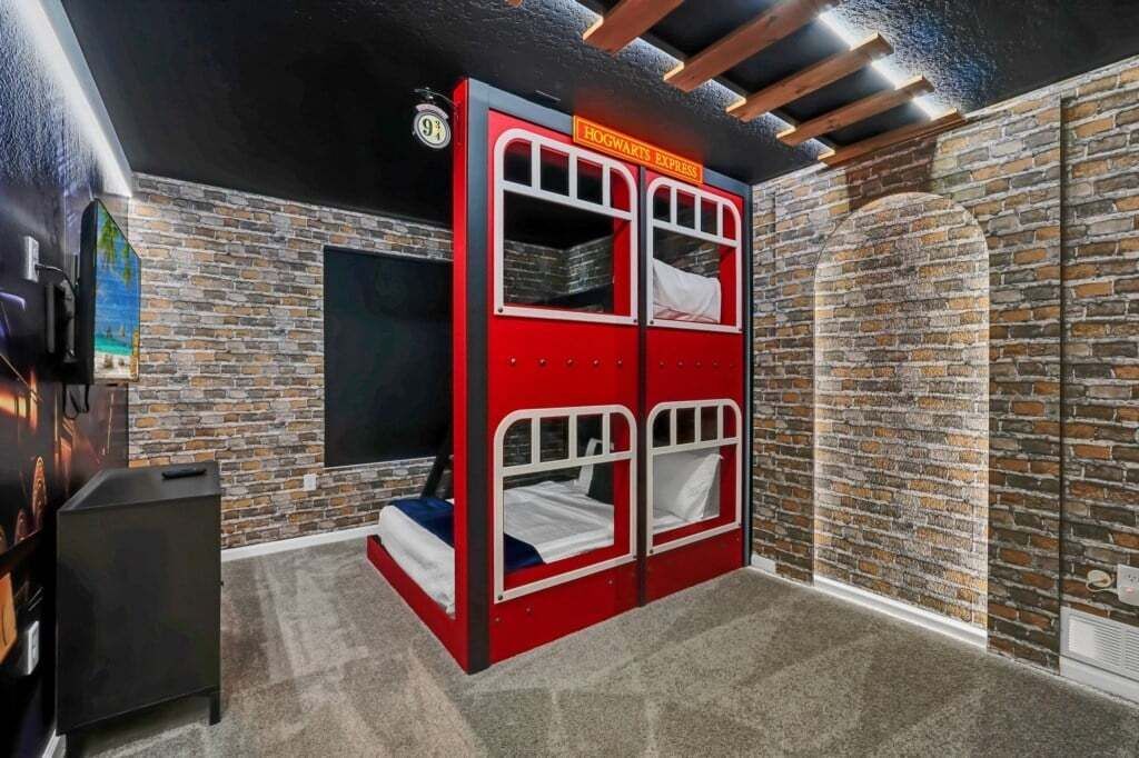 Een kamer met een rode stapelbed met daarop de tekst 'Hogwarts Express', een bakstenen muur, een kleine televisie en een vloerbedekking.
