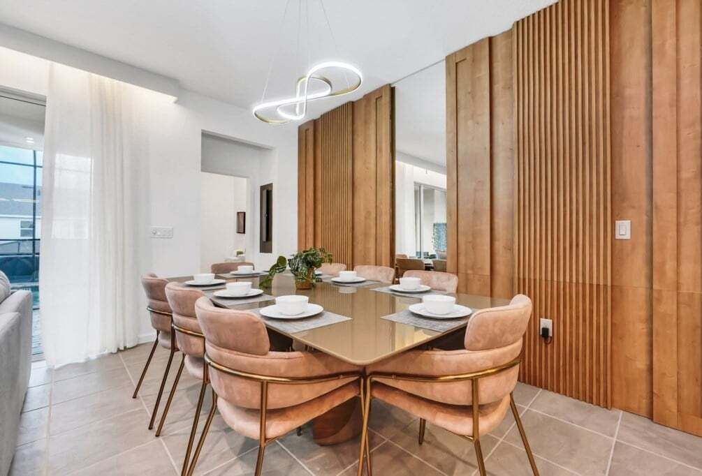 Un comedor moderno con una mesa de vidrio, sillas acolchadas y una pared de madera decorativa.