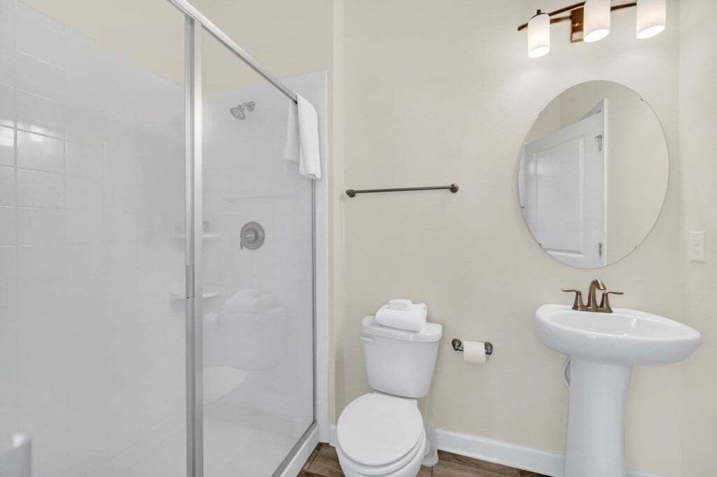 A bathroom with a glass shower enclosure, a toilet, and a pedestal sink.