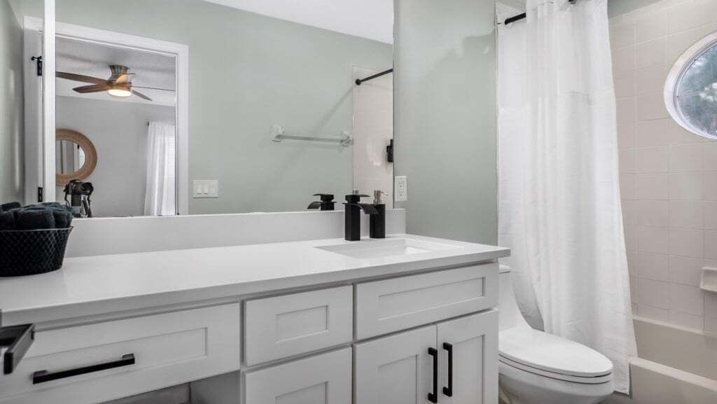 Une salle de bain avec un meuble-lavabo blanc, des toilettes, un rideau de douche et un ventilateur de plafond.