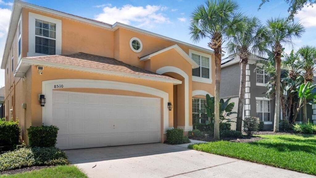 A two-story house with a garage, palm trees, and a well-maintained lawn.