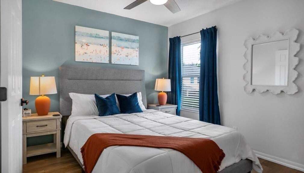 Un dormitorio con una cama, dos mesitas de noche, un ventilador de techo y una ventana con cortinas.