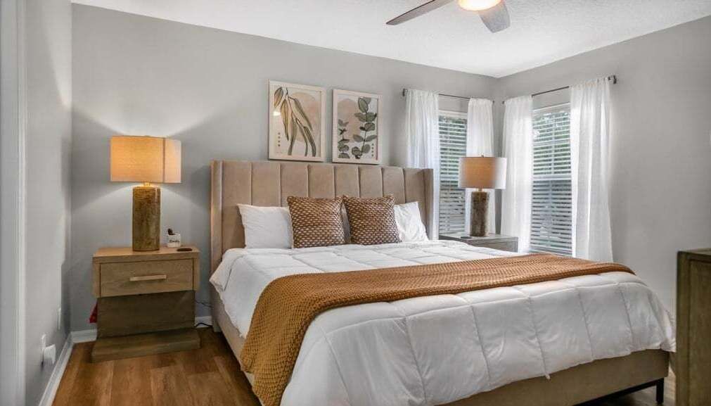 Une chambre à coucher comprenant un lit, des tables de chevet, un ventilateur de plafond et des œuvres d’art murales.