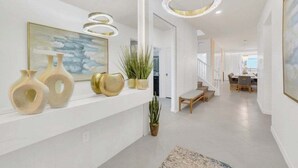 Moderni eteinen, jossa on valkoiset seinät, portaikko ja taustalla ruokailutila.