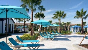 A poolside area with lounge chairs and umbrellas, palm trees, and a clear sky. - Beautiful Tranquil Relaxing Home With Private Pool 4 Bedroom Townhouse (Kissimmee)