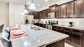 A modern kitchen with granite countertops, dark wooden cabinets, stainless steel appliances, and pendant lighting. - Beautiful Tranquil Relaxing Home With Private Pool 4 Bedroom Townhouse (Kissimmee)