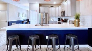 A modern kitchen with a large island, bar stools, stainless steel appliances, and pendant lighting. - Beautiful 8 Bed Home In Champions Gate-303oc 8 Bedroom Home (Davenport)