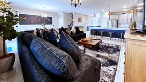 A modern living room with a sofa, coffee table, and a large plant. There is a staircase leading to another level. - Beautiful 8 Bed Home In Champions Gate-303oc 8 Bedroom Home (Davenport)