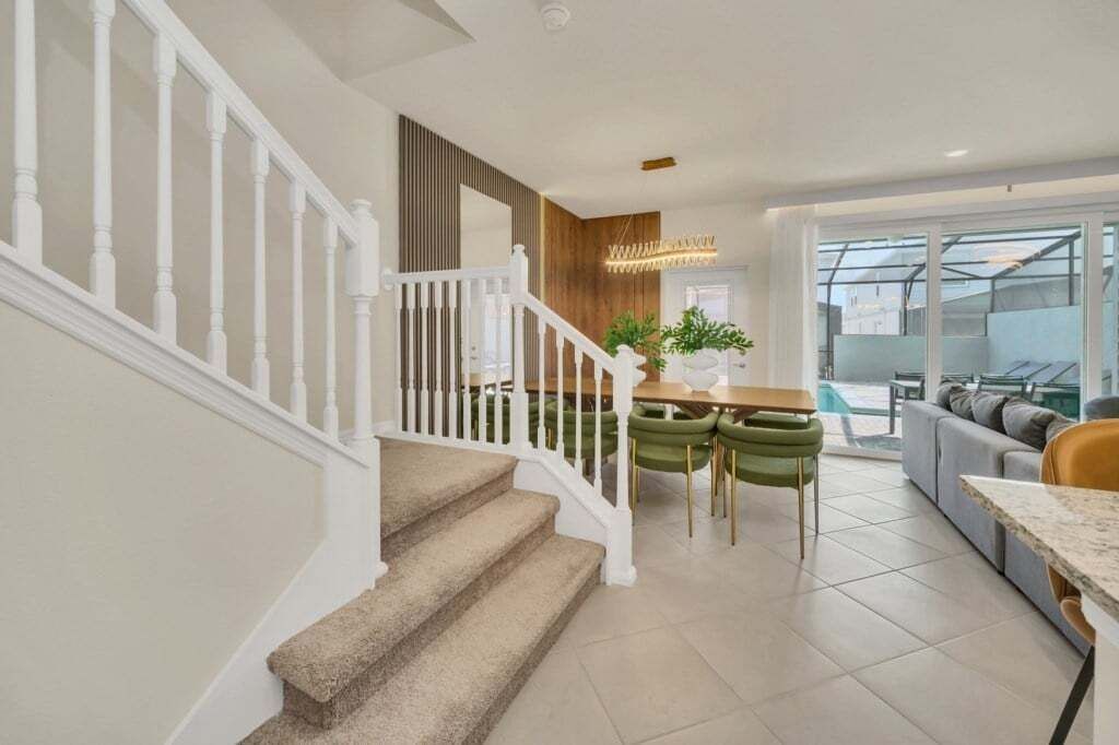 A modern interior with a staircase, a dining area with green chairs, and a large window.