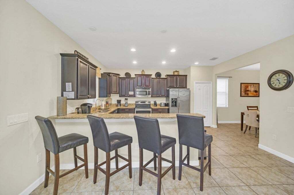 A kitchen with dark wooden cabinets, a central island with bar stools, and a dining area with a table and chairs.