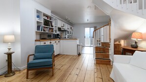 A modern kitchen with white cabinetry, a blue chair, and a wooden staircase. - 6 Village Edge 2 Bedroom Condo (Warren)