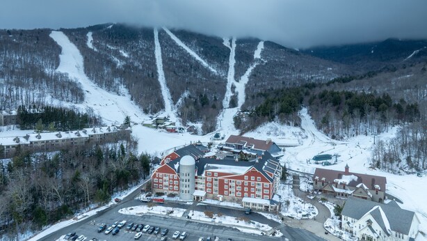 A large, red-brick building with a central tower, surrounded by a parking lot and snow-covered hills. - 6 Village Edge 2 Bedroom Condo (Warren)
