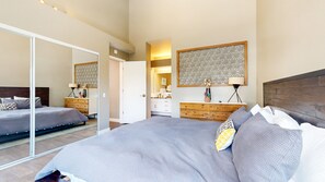 A bedroom with a large bed, a wardrobe, a bedside table, a mirror, and a decorative wall panel. - Snowcreek V #888 3 Bedroom Condo (Mammoth Lakes)