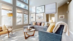 A modern living room with a grey sofa, a round coffee table, and a large window with blinds. - Snowcreek V #888 3 Bedroom Condo (Mammoth Lakes)