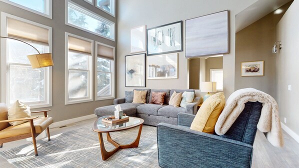 A modern living room with a grey sofa, a round coffee table, and a large window with blinds. - Snowcreek V #888 3 Bedroom Condo (Mammoth Lakes)