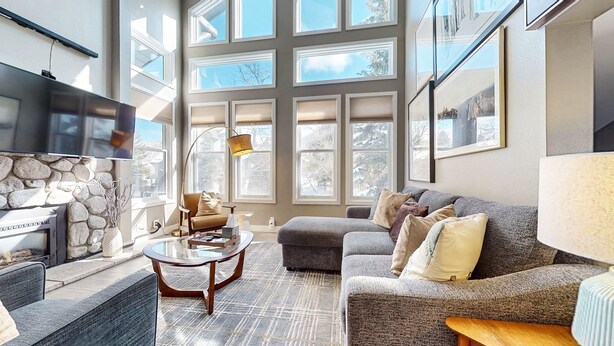 A spacious living room with a stone wall, large windows, a flat-screen TV, and a comfortable seating area. - Snowcreek V #888 3 Bedroom Condo (Mammoth Lakes)