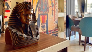 Habitación con un gran mural egipcio, un busto sobre una mesa y una zona de comedor moderna con sillas y una mesa.